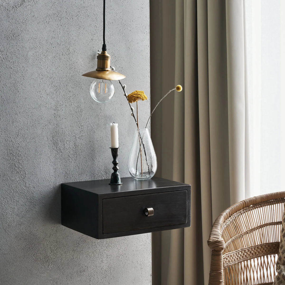Small black wall-mounted drawer or nightstand with a lamp, candle, and vase against a grey wall.