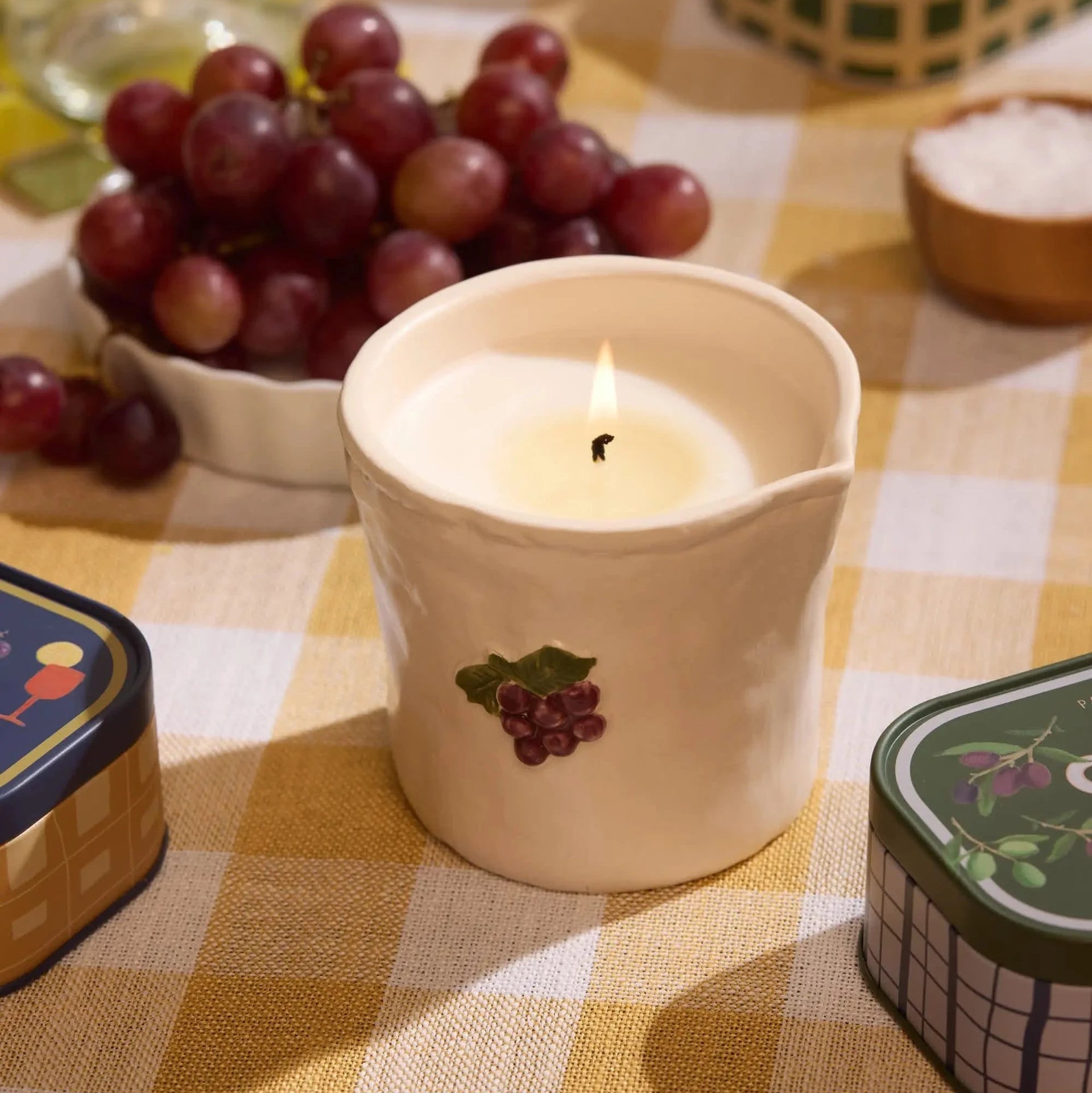 Candle in a decorative holder with grapes on a checkered tablecloth
