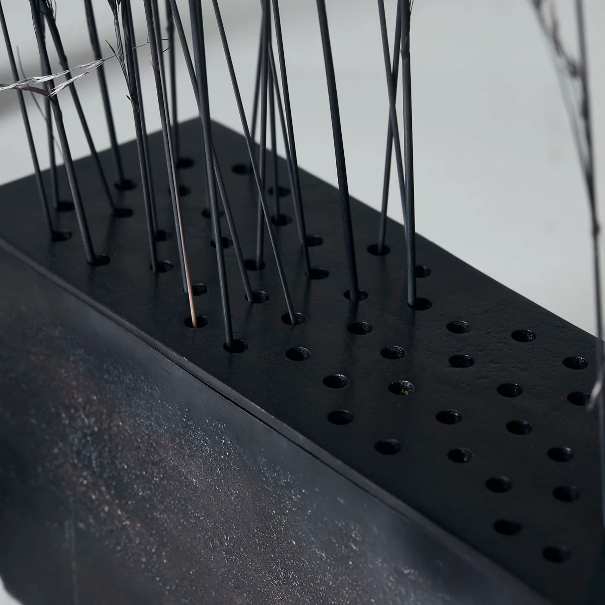 Black rectangular metal vase with small holes to put individual stems in closeup