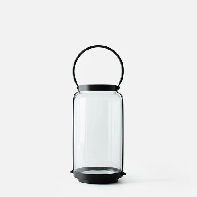 Clear glass lantern with black metal handle on a white background