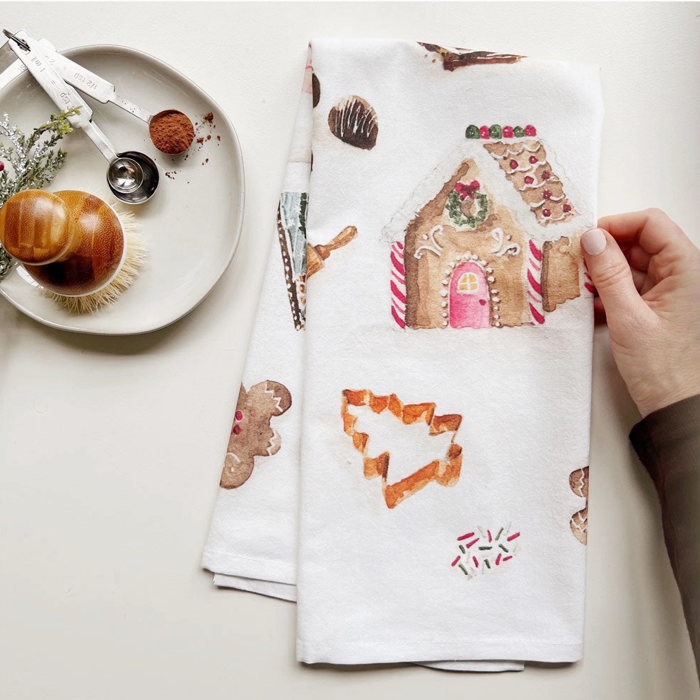 White towel with gingerbread house and cookie designs held by a hand on a light background.