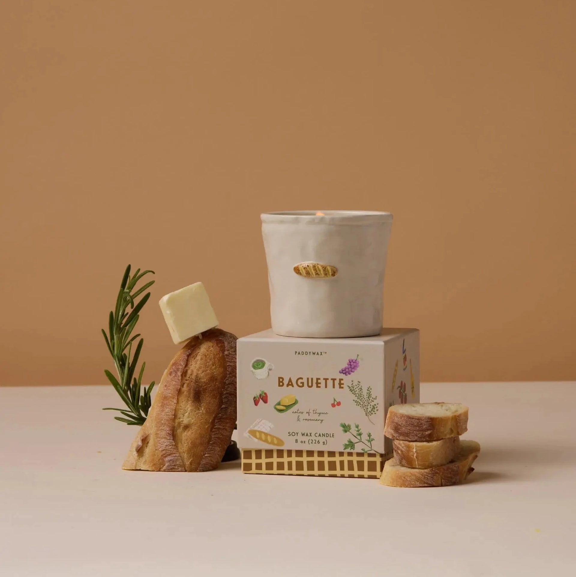 Candle, baguette, and box on a beige surface with a brown background